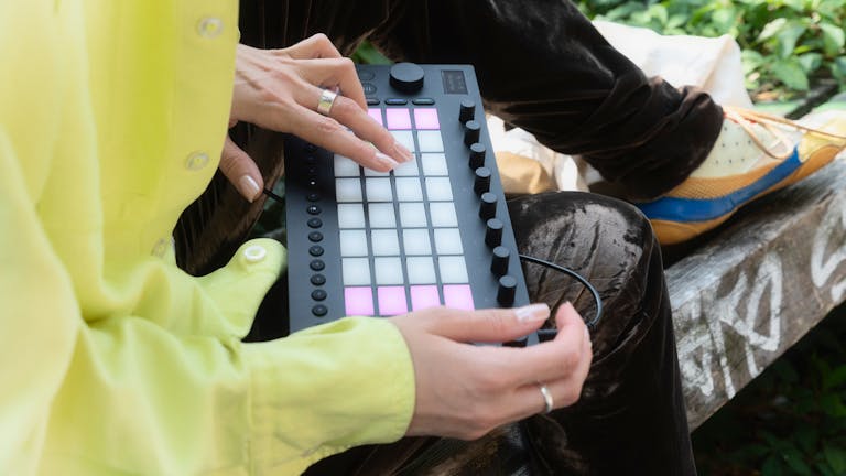 Vista lateral de una persona tocando Ableton Move mientras está sentada al aire libre.
