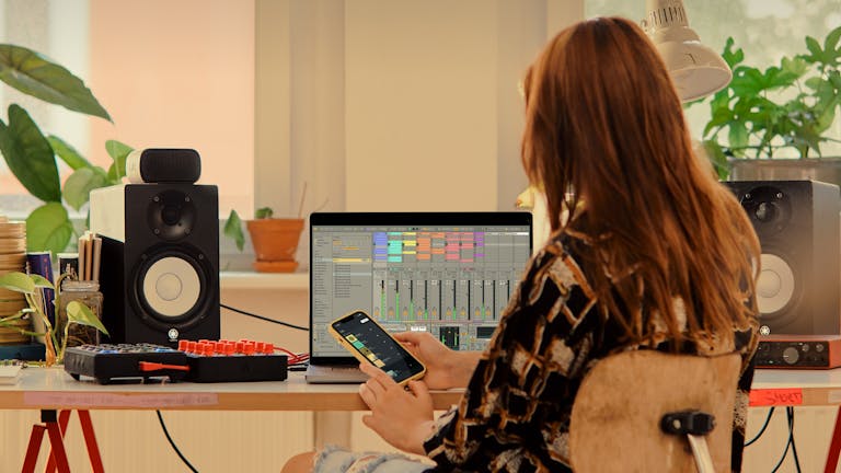 Una música sentada en la mesa de su estudio, usando Ableton Note con Ableton Live Lite asoleándose en su portátil.